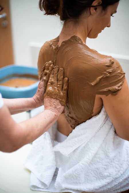 Bad Camberger Lehm wird auf dem Rücken einer Frau aufgetragen